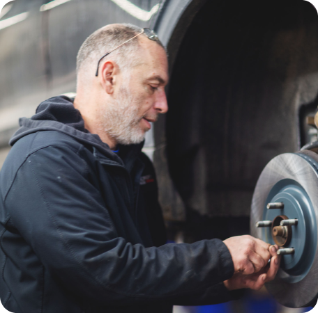 Mechanic in a dark jacket inspecting a car brake assembly in a garage | Browncroft Garage