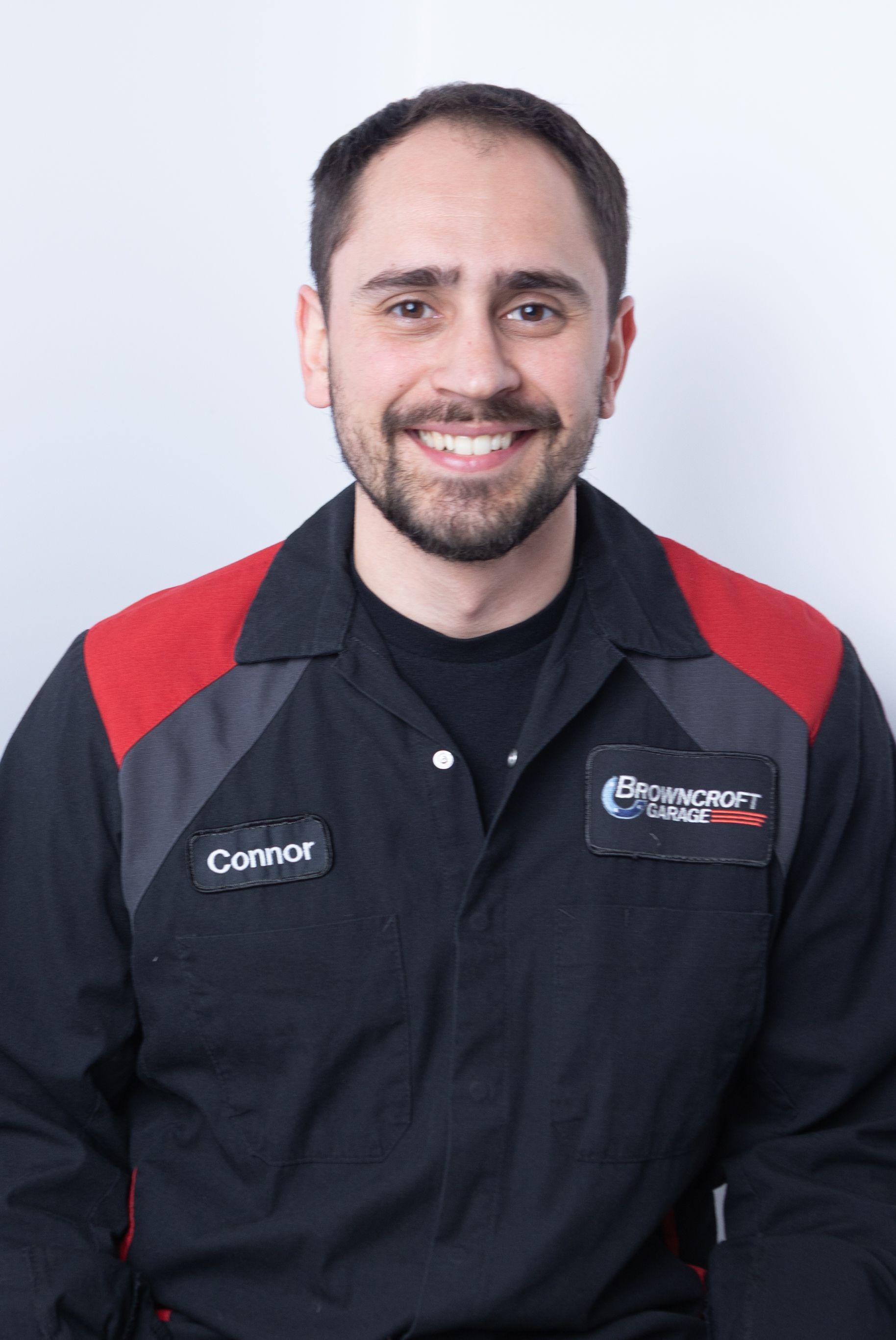Smiling mechanic in black and red uniform standing against a light background | Browncroft Garage