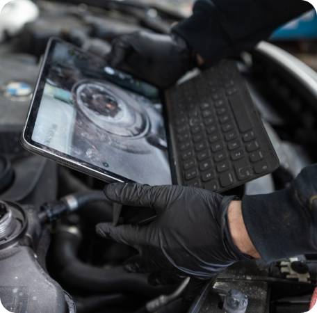 Gloved hands using a tablet with a keyboard on a motorcycle engine for diagnostics | Browncroft Garage