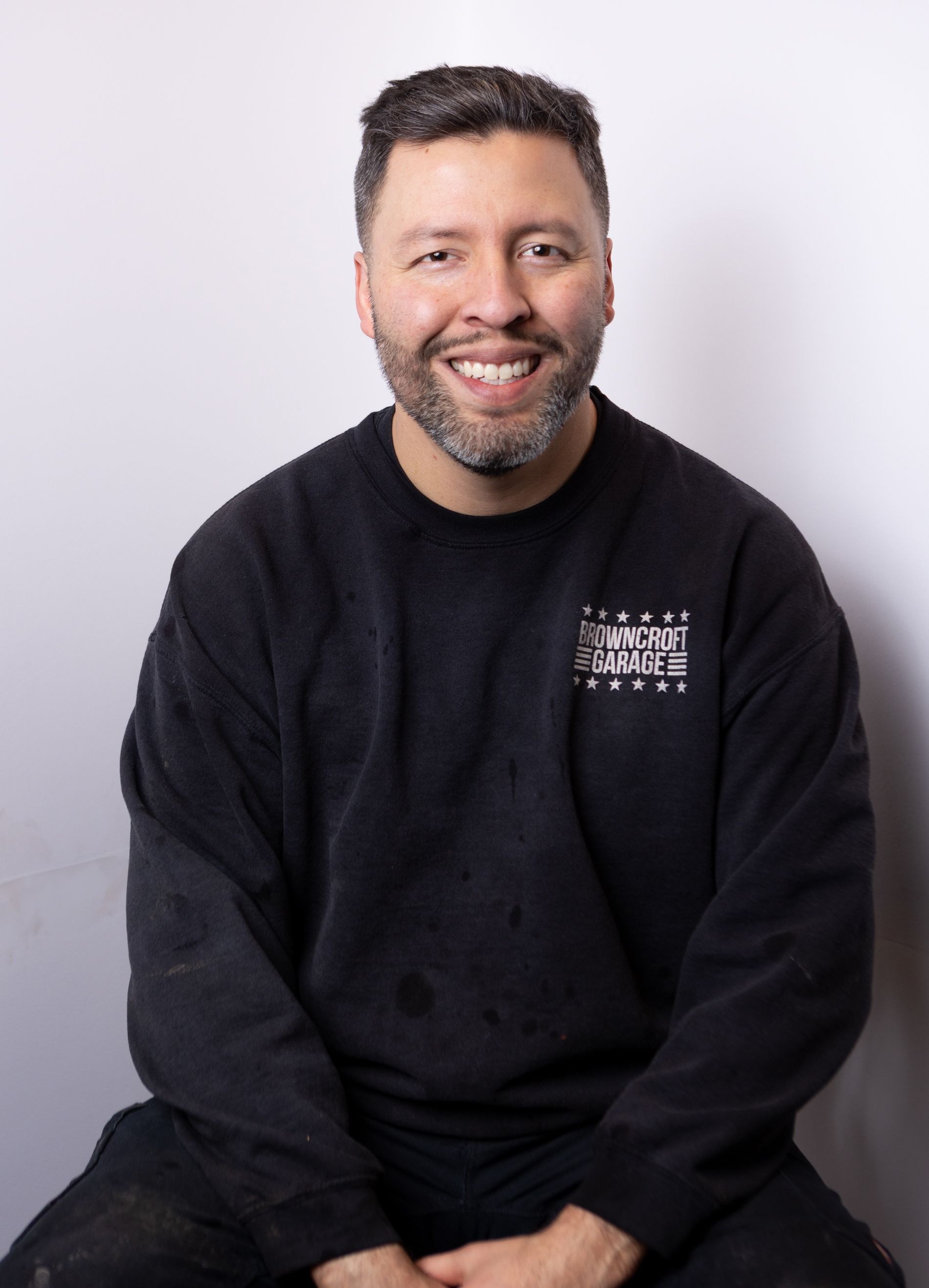 Smiling man in a black sweatshirt seated against a light background | Browncroft Garage