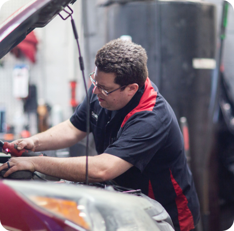 Mechanic in black and red shirt working under a car hood in an auto shop | Browncroft Garage