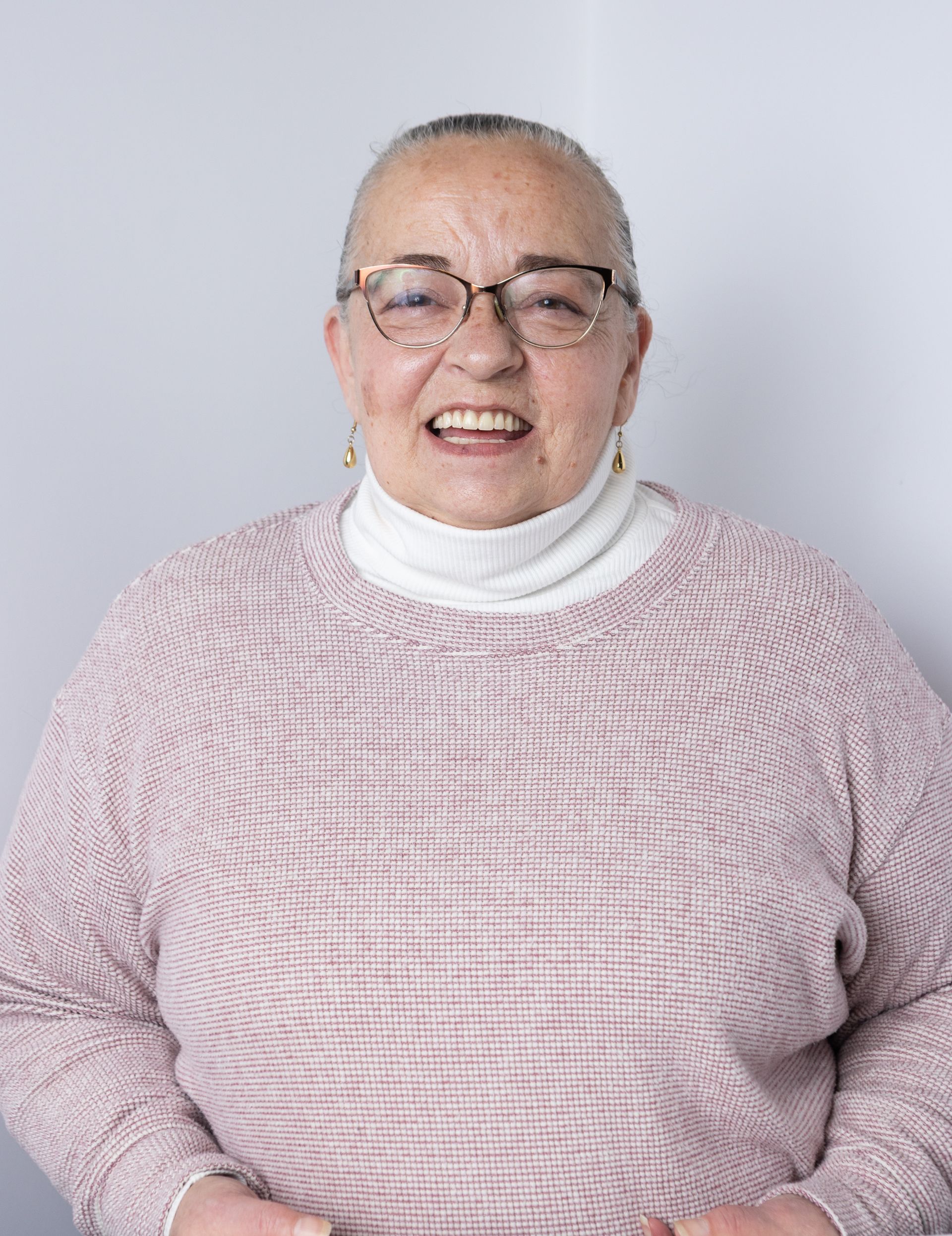 Smiling person in glasses wearing a pink sweater against a light gray background | Browncroft Garage