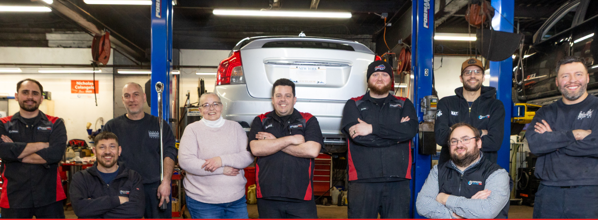 Group of mechanics in a garage posing in front of a white van on lifts | Browncroft Garage