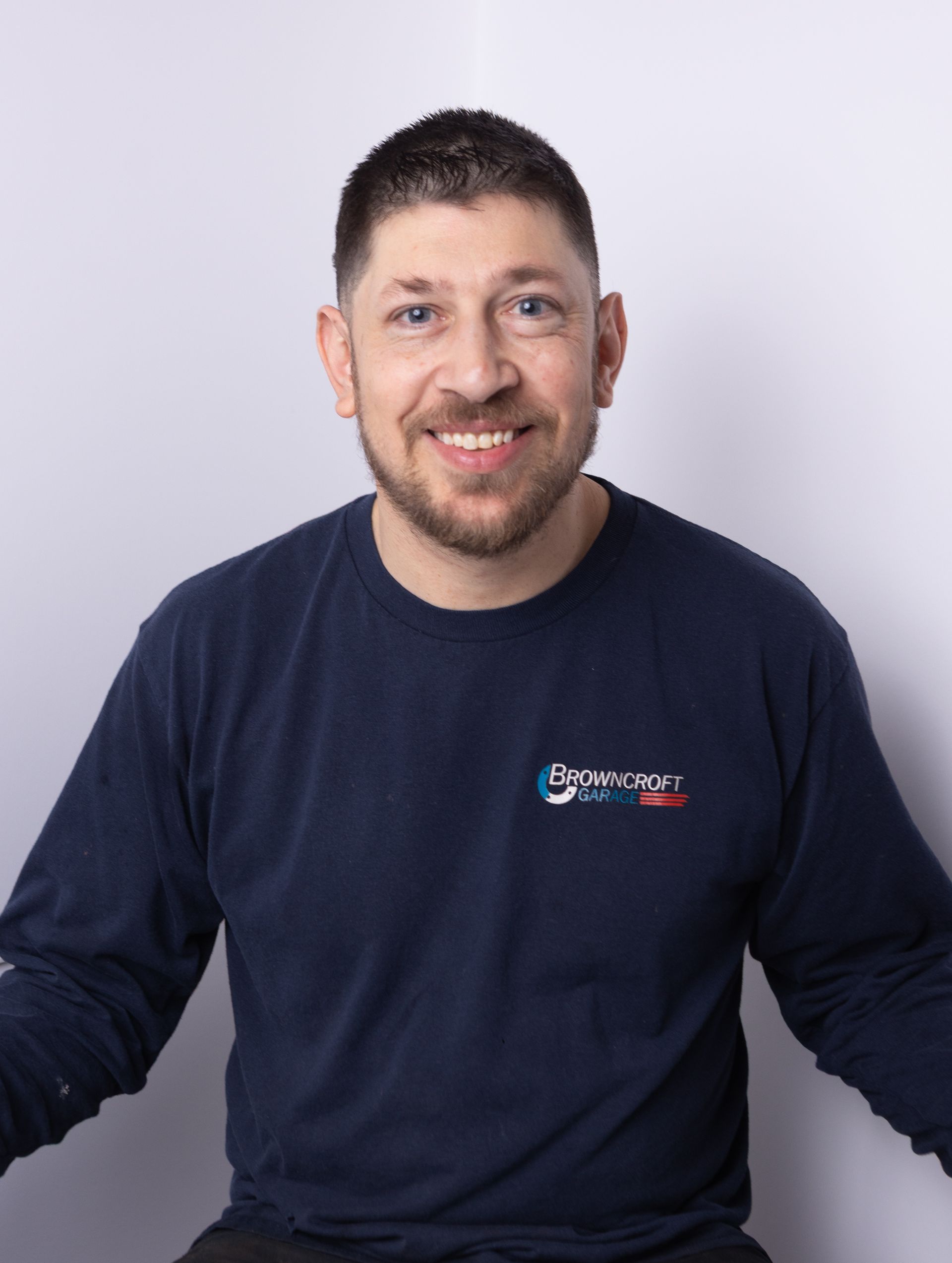 Smiling man in a navy long-sleeve shirt against a light background | Browncroft Garage