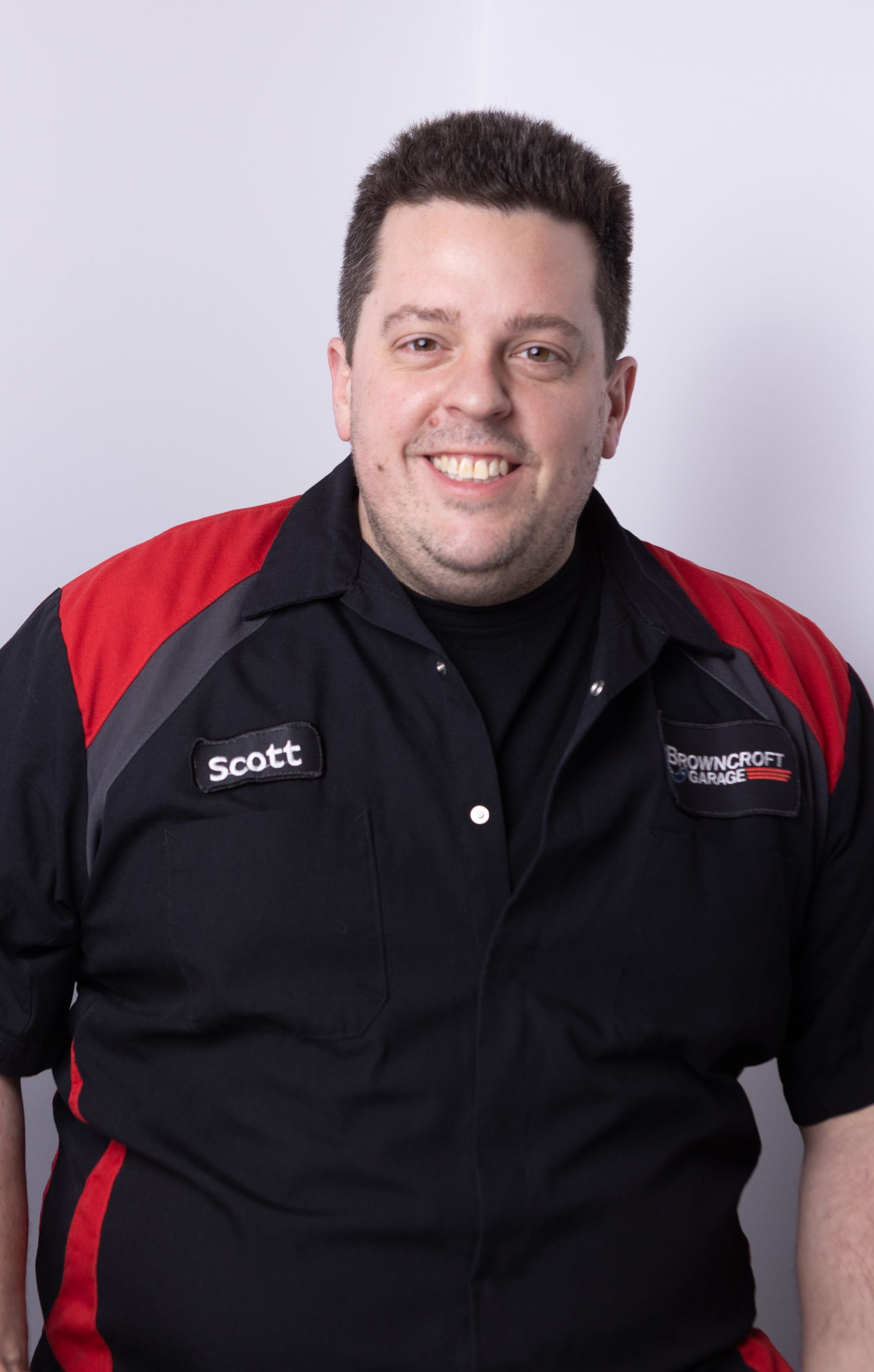 Man smiling in a black shirt with red accents, standing against a light background. | Browncroft Garage