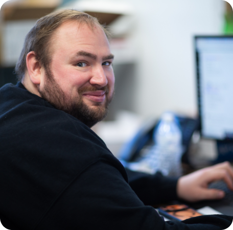 Man seated at a desk, smiling over his shoulder at the camera in an office setting. | Browncroft Garage
