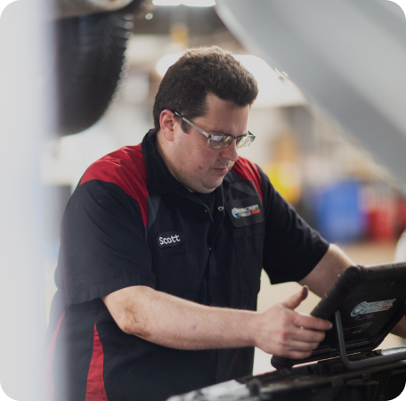 Technician in a black and red uniform working on a tablet in a workshop | Browncroft Garage