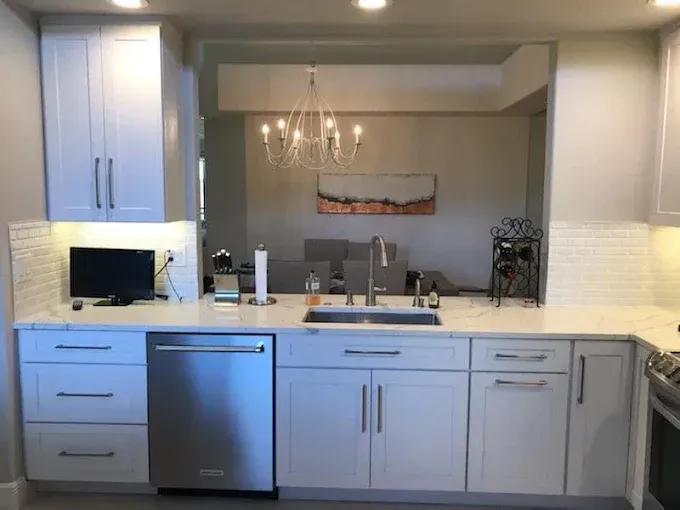 A modern kitchen featuring white cabinets, stainless steel appliances, and a pass-through opening to a dining area.