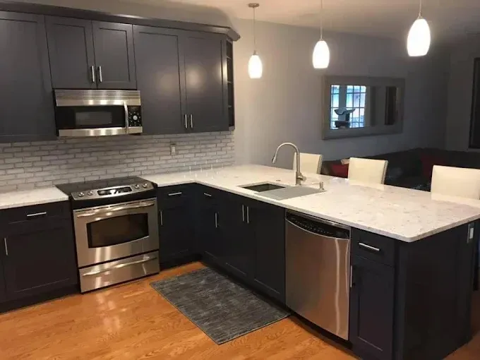 Modern kitchen with dark navy cabinets, white countertops, stainless steel appliances, and a central island with seating.