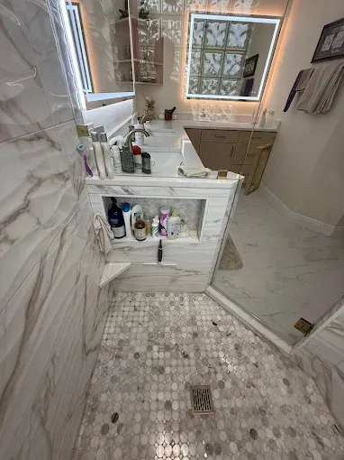 A bathroom featuring a shower with pebble flooring, a marble-tiled wall, and a built-in shelf stocked with toiletries.