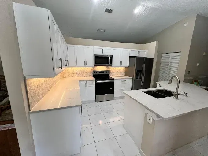 A modern kitchen with white cabinets, light countertops, stainless steel appliances, and tile flooring.