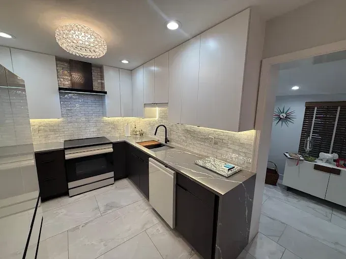 Modern kitchen with white upper cabinets, dark base cabinets, marble-patterned countertops, and a stone backsplash.