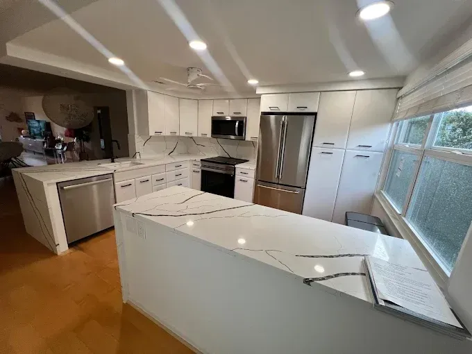 Modern kitchen with white cabinets, stainless steel appliances, and a marble-patterned island countertop.