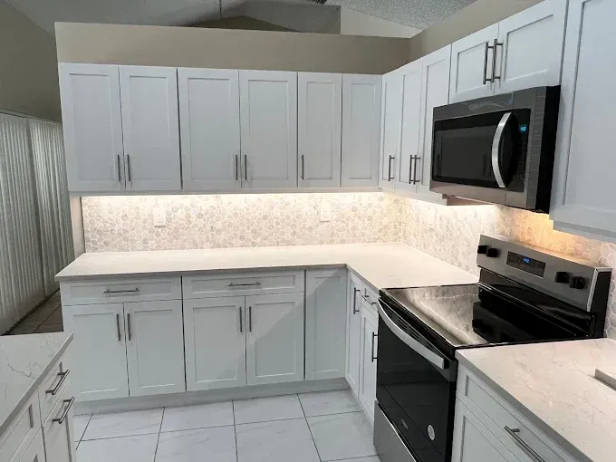 Modern kitchen with white shaker-style cabinets, white countertops, marble-patterned backsplash, and stainless appliances.