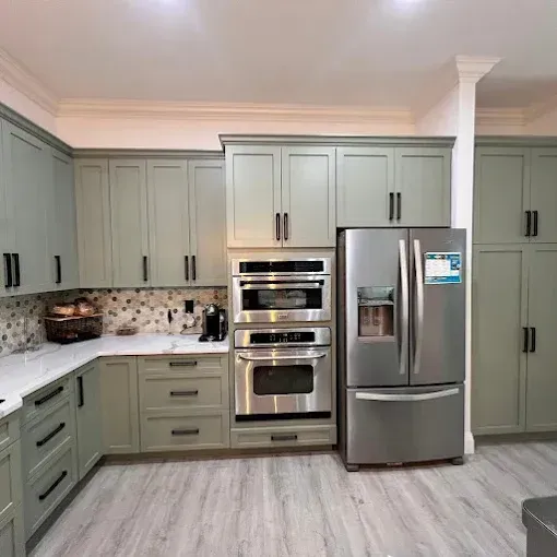 A modern kitchen with sage green cabinets, white marble countertops, stainless steel appliances, and a tiled backsplash.