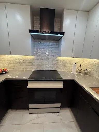 A modern kitchen featuring white upper cabinets, dark base cabinets, a black stove, and a white brick-style backsplash.