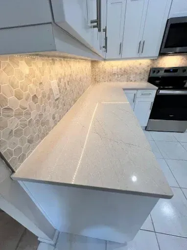 A high-angle view of a white modern kitchen counter with a light quartz top and tan hexagonal tile backsplash.