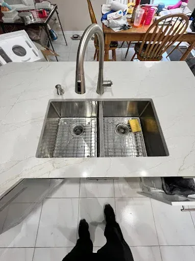 A modern kitchen island with a double stainless steel sink and tall gooseneck faucet, viewed from above.