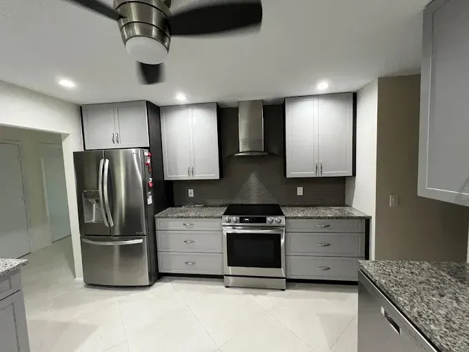 A modern kitchen featuring gray cabinets, stainless steel appliances, speckled granite countertops, and a ceiling fan.