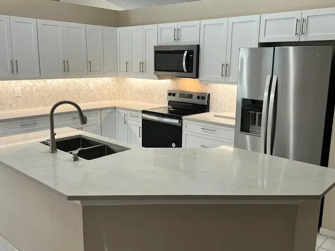 A modern kitchen featuring white shaker cabinets, white countertops, stainless steel appliances, and a central island.