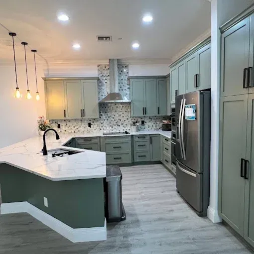 Modern kitchen with sage green cabinets, white quartz countertops, a stone-patterned backsplash, and stainless appliances.