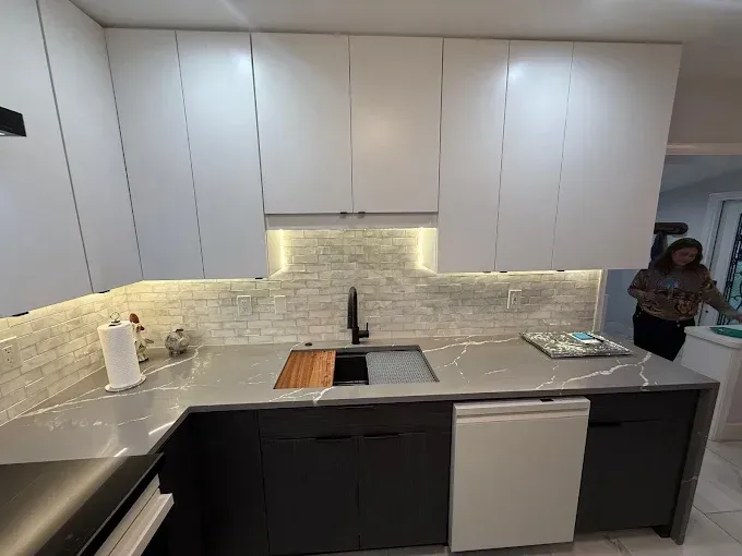 Modern kitchen with white upper cabinets, dark lower cabinets, marble-patterned countertops, and tiled backsplash.