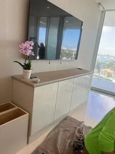 A light-colored cabinet stands beneath a wall-mounted television, featuring a potted orchid on its surface.