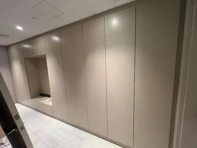 A wall of tall, light-tan cabinetry featuring a built-in alcove, positioned above a white marble floor.