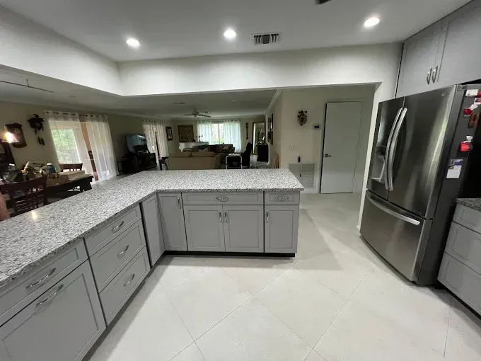 A spacious kitchen with light gray cabinets, speckled granite countertops, and a stainless steel refrigerator.