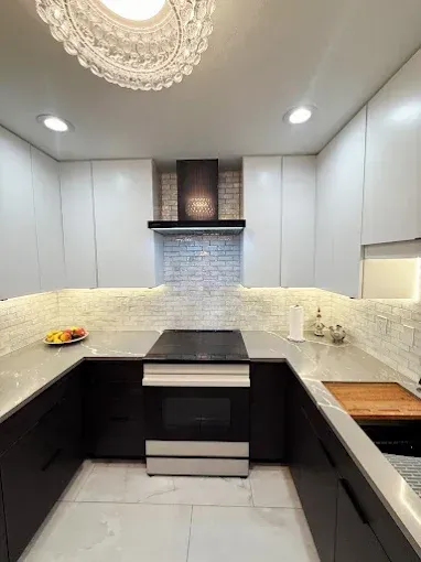 A modern u-shaped kitchen featuring white upper cabinets, dark base cabinets, a stone backsplash, and a central range.