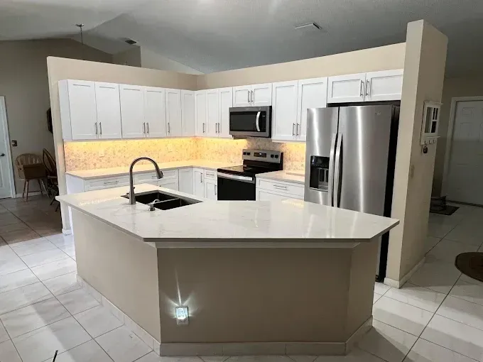 A kitchen with white cabinets, a peninsula counter, stainless steel appliances, and under-cabinet lighting.
