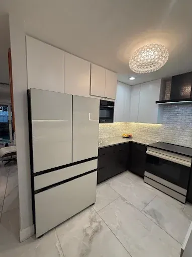 A modern kitchen features a tall, light-grey refrigerator, dark lower cabinets, white upper cabinets, and marble flooring.