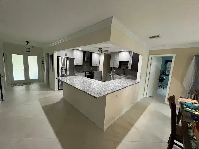 Open-concept kitchen with a granite island, white cabinets, stainless steel appliances, and beige tile floors.