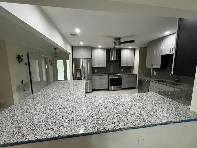 Modern kitchen featuring grey cabinets, stainless steel appliances, and a large speckled granite peninsula countertop.