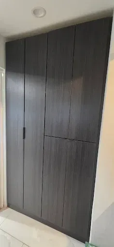 A floor-to-ceiling wooden wardrobe with dark brown vertical wood grain and a matte black handle.