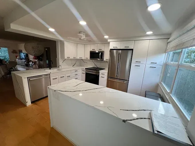 Modern white kitchen featuring a marble-patterned island, stainless steel appliances, and wood floors.