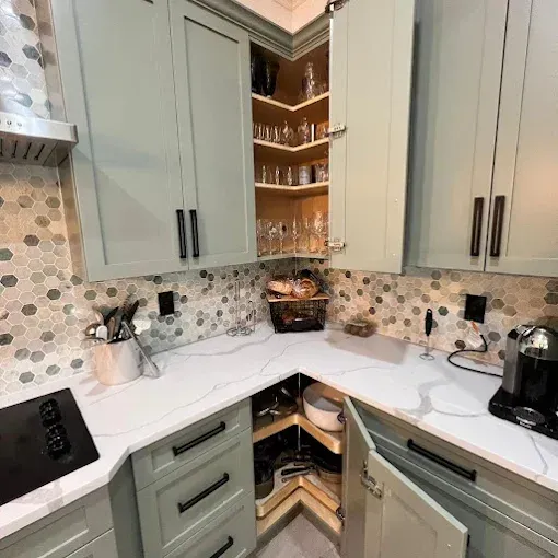 A corner kitchen with sage green cabinets, white marble-patterned countertops, and a honeycomb-patterned backsplash.