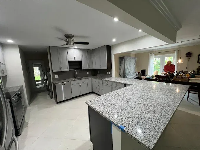A modern kitchen featuring gray cabinets, speckled granite countertops, stainless appliances, and an open dining area.