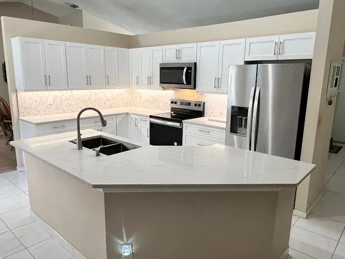 Modern kitchen with a white, L-shaped island, white cabinets, stainless steel appliances, and a light-colored backsplash.