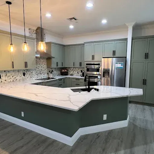 Modern kitchen featuring sage green cabinets, white marble countertops, stainless appliances, and three pendant lights.