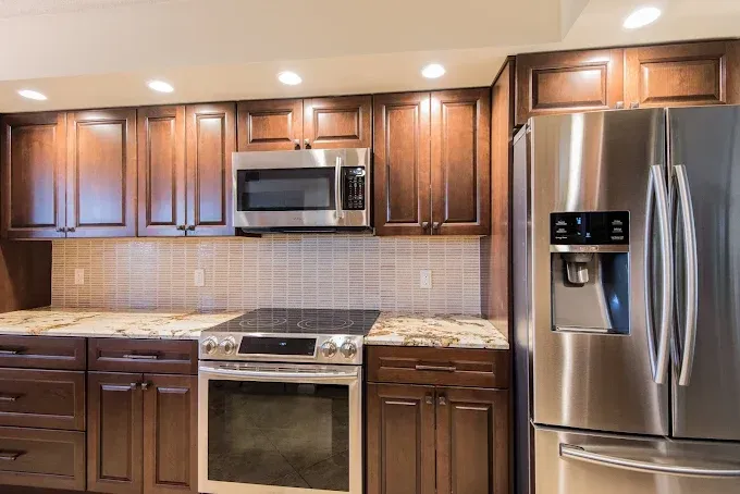 A kitchen featuring dark wood cabinets, a stainless steel microwave, oven, and refrigerator with a tiled backsplash.