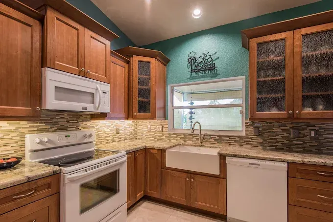 A kitchen with wood cabinets, white appliances, a farmhouse sink, and teal walls featuring a decorative metal wine rack.
