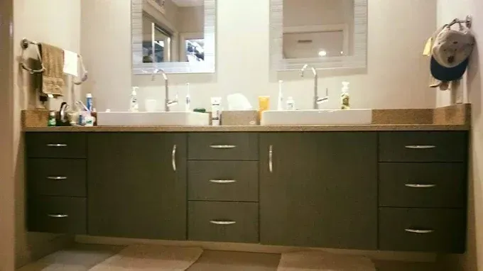 A double vanity with dark green cabinets, two white sinks, and two rectangular mirrors in a neutral-toned bathroom.