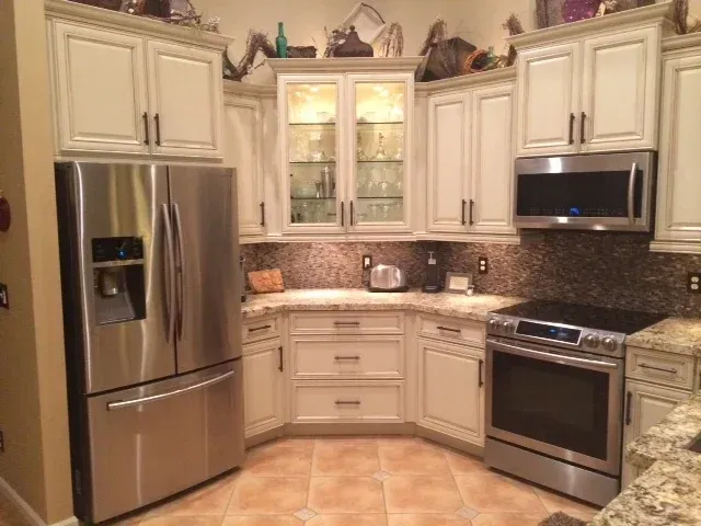 A modern kitchen featuring off-white cabinets, stainless steel appliances, a glass-front display cabinet, and tiled floors.
