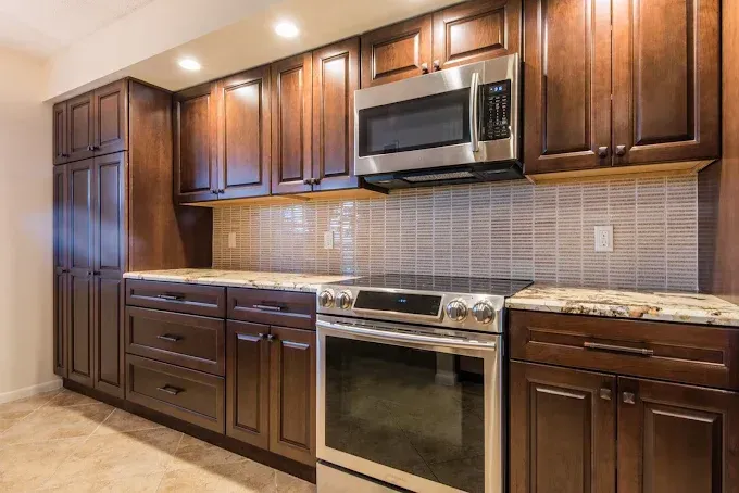 A kitchen featuring dark wood cabinets, a stainless steel oven and microwave, granite countertops, and tiled backsplash.