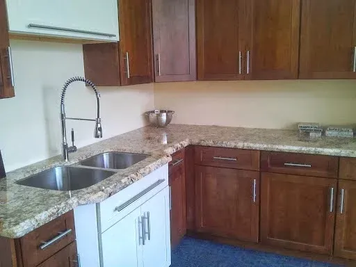 A kitchen featuring brown wood cabinets, granite countertops, a double-basin stainless steel sink, and a high-neck faucet.