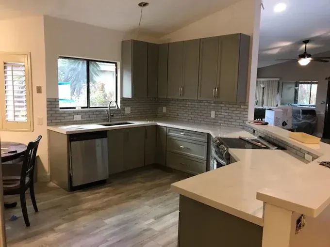 A modern kitchen with grey cabinets, white countertops, stainless steel appliances, and wood-look flooring.