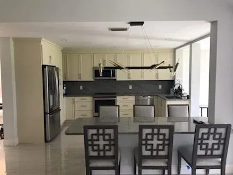 A modern kitchen features light-colored cabinetry, a dark grey backsplash, stainless appliances, and a central dining island.