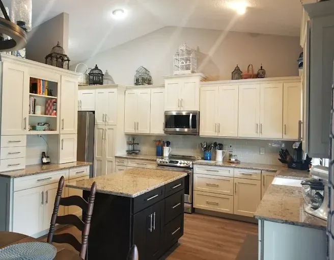 A bright kitchen with white cabinets, a dark brown island, granite countertops, and stainless steel appliances.