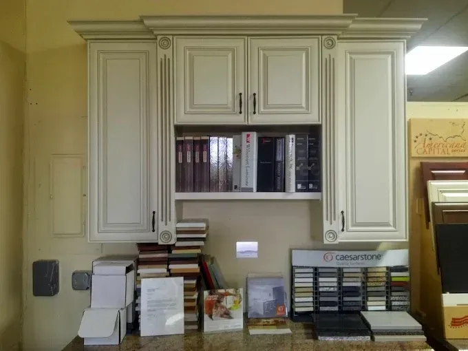 Cream-colored kitchen cabinets with decorative columns and an open middle shelf, displayed in a store with material samples.